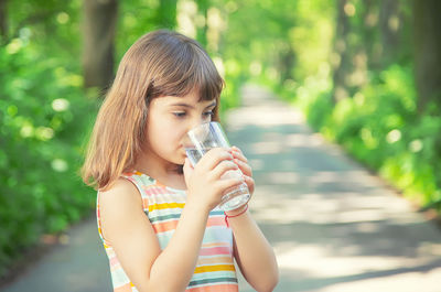 Cute girl drinking water while standing outdoors