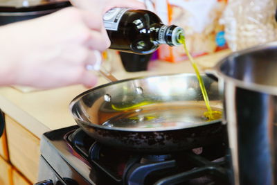 Cropped hand pouring olive oil in cooking utensil over stove at home
