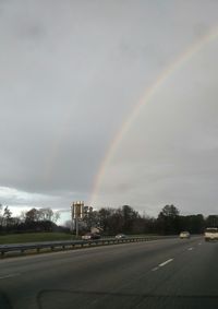 Road passing through city against cloudy sky