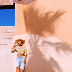 Portrait of woman wearing hat standing against wall outdoors