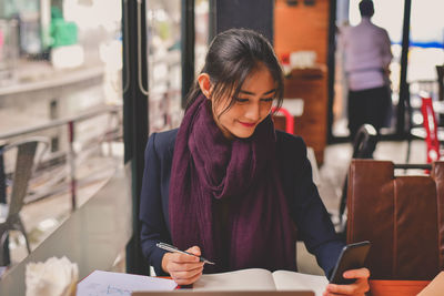 Young woman looking through smart phone while sitting on laptop