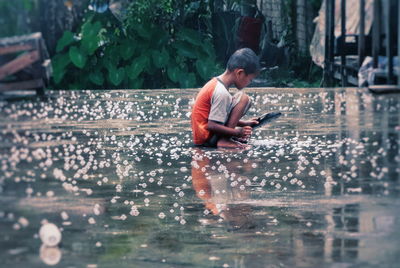 Side view of boy using mobile phone in water