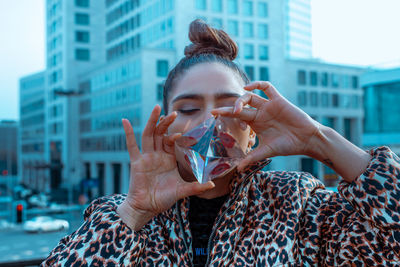 Close-up of woman with mouth open reflecting on crystal against buildings in city