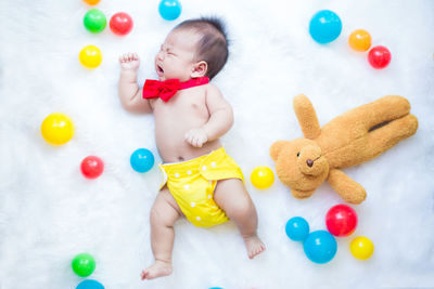 High angle view of shirtless baby boy crying while lying on bed