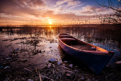 Boat moored at shore against sky during sunset