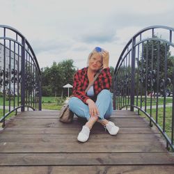 Young woman sitting on railing against bridge