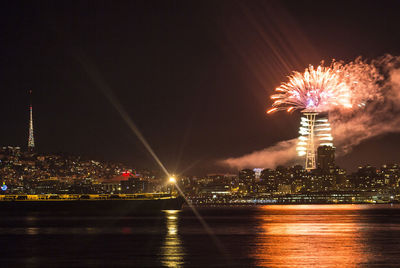 Firework display over illuminated city against sky at night