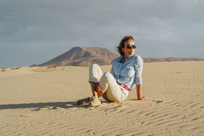 Full length of woman sitting on sand in desert against sky