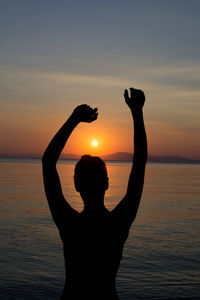 Silhouette person standing by sea against sky during sunset