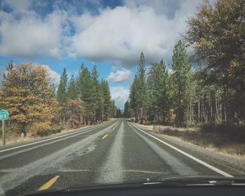 Road amidst trees against sky seen through car windshield