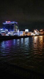 Illuminated cityscape by sea against sky at night