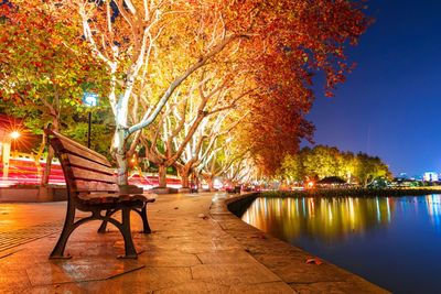 Sidewalk in park by lake against sky during autumn