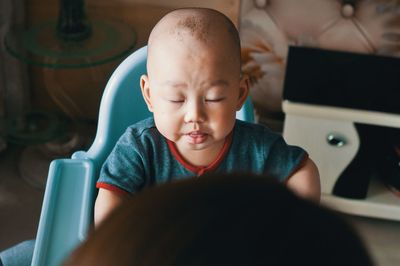 Cute baby boy with eyes closed sitting on high chair at home