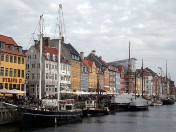 Boats moored at harbor against sky in city