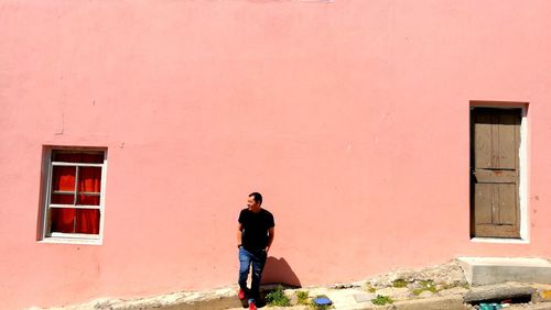 Full length of man leaning on pink wall