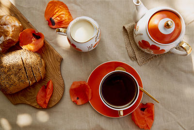 Traditional poppy seed bun, tea cup and milk near poppies flowers and dishes with poppies ornaments