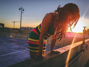 Woman with umbrella on street against sky during sunset