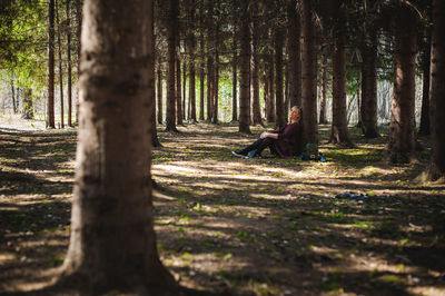 Portrait of woman sitting by tree trunk in forest