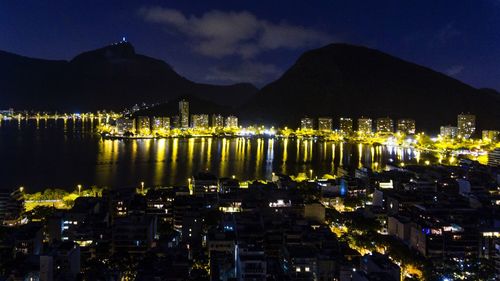 Illuminated cityscape by sea against sky at night