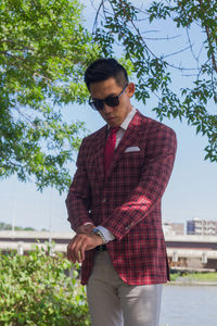 Portrait of young man wearing sunglasses standing against trees