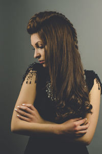 Young woman looking away while standing against gray background