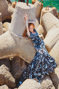 Full length portrait of young woman lying on rock by sea