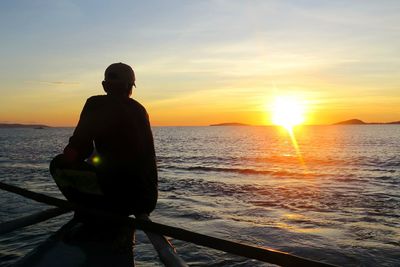 Rear view of silhouette man on shore against sunset sky