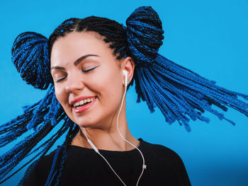 Close-up of young woman listening to headphones against colored background