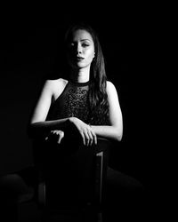 Young woman looking away while sitting on chair against black background