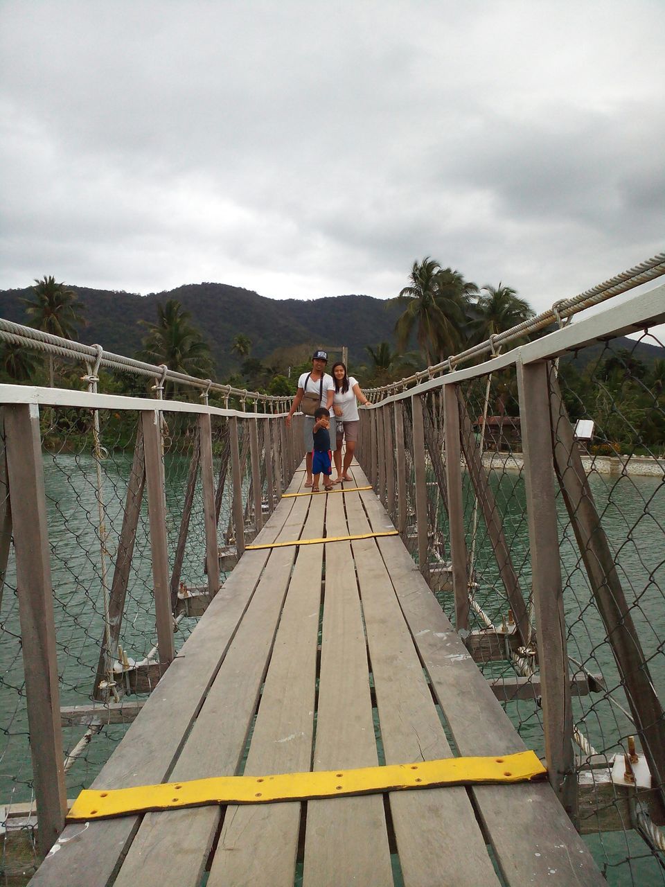 sky, railing, mountain, cloud - sky, leisure activity, lifestyles, full length, water, connection, bridge - man made structure, rear view, footbridge, built structure, men, tranquility, pier, the way forward, cloud