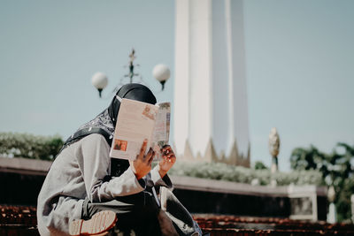 Woman reading magazine while sitting outdoors during sunny day