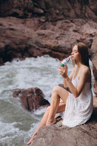Young woman drinking water on rock