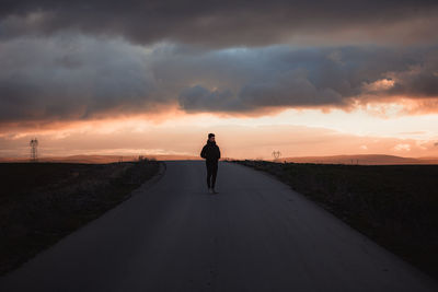 Rear view of man standing on road against sky during sunset