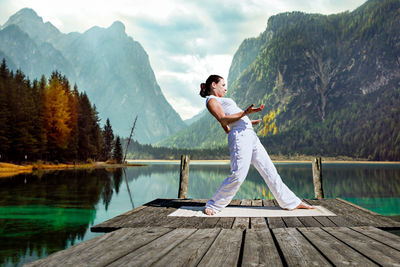 Woman exercising while standing on pier by lake