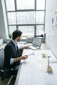 High angle view of businessman using laptop while holding wind turbine models