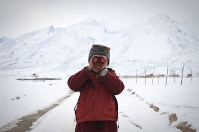 Boy looking through binoculars against snowcapped mountains