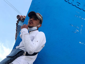 Low angle view of young man standing against blue sky