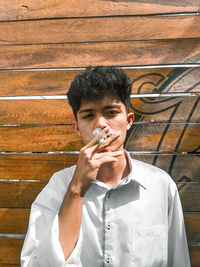 Young man smoking cigarette against wall