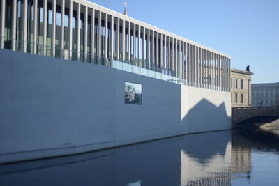 Bridge over river by building against clear blue sky