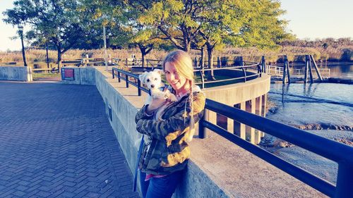 Portrait of smiling young woman with dog standing by railing