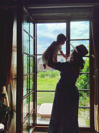 Side view of woman standing by window at home