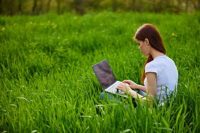 Young woman using laptop while sitting on field