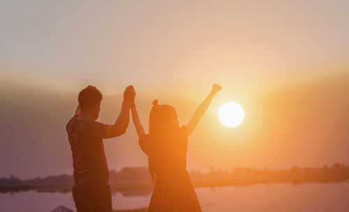 Friends standing on shore against sky during sunset