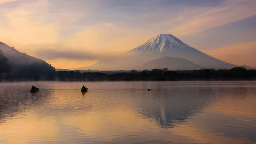 Scenic view of lake by snowcapped mountains against sky during sunset