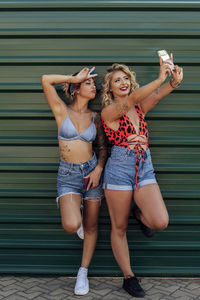 Friends taking selfie through smart phone in front of green metal wall