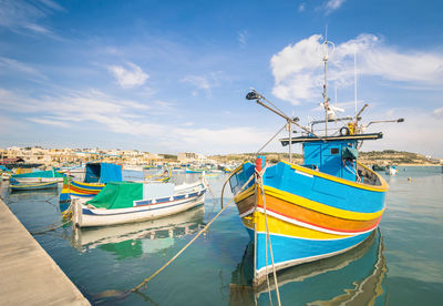 Fishing boats moored at harbor against sky