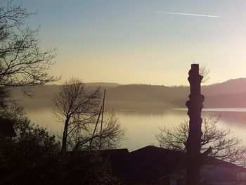 Silhouette bare tree by lake against clear sky