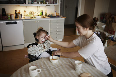 Mother feeding disabled child in wheelchair at home