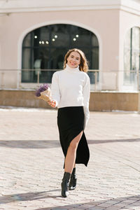 Young caucasian woman holds a purple bouquet of flowers in her hands and walks along a city street