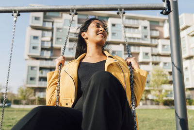 Playful young woman sitting on swing at playground